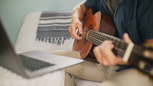 istock Person, hand and guitar with laptop for online learning on internet for virtual lesson, live streaming or performance. Artist, fingers and instrument on sofa for at home education, practice or music 1995179274