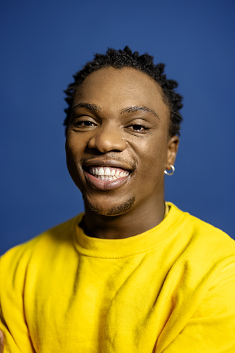 Close-up portrait of smiling young man looking at camera against blue background. Handsome man wearing t-shirt in studio.