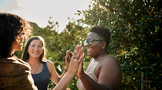 Laughing woman and a group of other women standing with her hands together during an exercise at a wellness retreat in summer