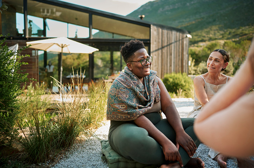 Diverse group of women talking together while sitting around a meeting area set outside in a scenic wellness retreat