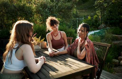Diverse group of women supporting each other while talking together around a patio table outside during a summer wellness retreat