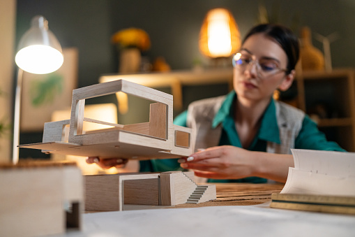 Young female architect making an architectural model in her home office.