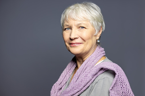 Portrait of a confident mature woman with short hair looking at camera. Beautiful senior woman looking happy against grey background.