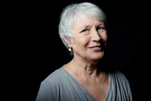 Close-up portrait of smiling senior woman looking at camera on black background. Happy elderly woman with short grey hair against black background.