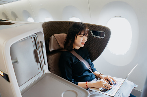 An Asian businesswoman entrepreneur traveling in business class and working with laptop on an airplane. Business travel and vacation concept.