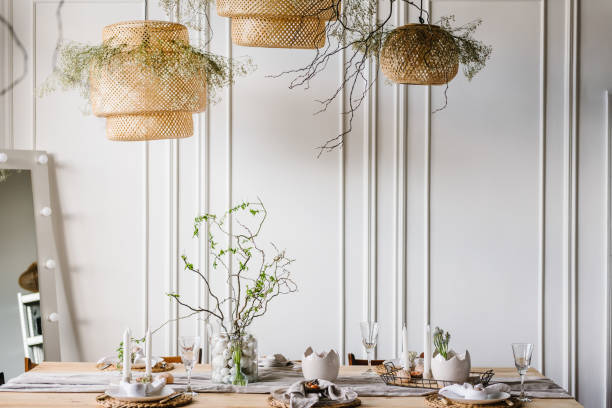 istock Interior design of easter dining room. Happy easter dinner with decor at home. Minimalist composition in living room with copy space, hanging lamp, candles, easter eggs, vase with twig, branch, leaves 1995229736