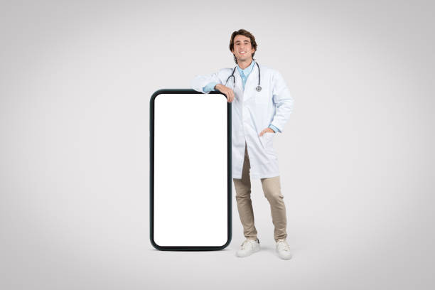 istock Smiling male doctor leaning on a blank smartphone screen, mockup 1995242072
