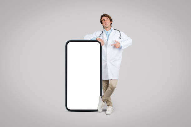 istock Doctor in lab coat leaning on a large phone, pointing at blank screen 1995242079