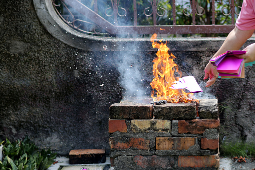 A senior Asian woman is burning offering papers (hell bank notes) for prayers