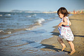 Barefoot toddler girl running on a beach toward sea water.