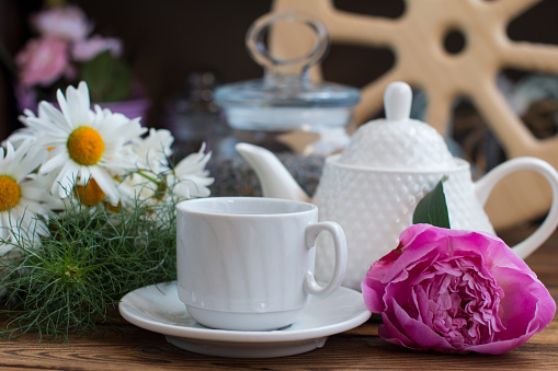 A cup of tea and a teapot with a rose on a wooden background with a wooden wheel. The concept of breakfast in the village