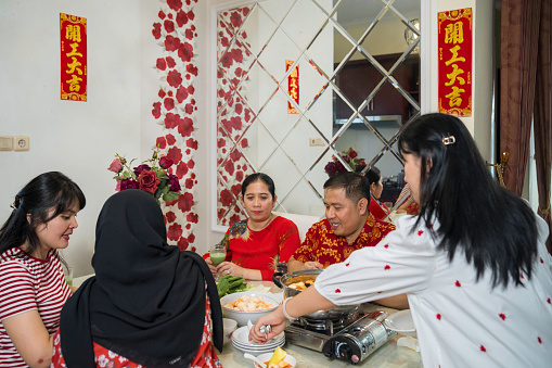 An extended family sitting at a dining table and eating a meal during Chinese New Year at home