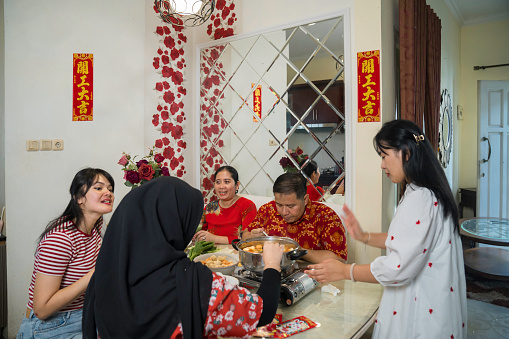An extended family sitting at a dining table and eating a meal during Chinese New Year at home