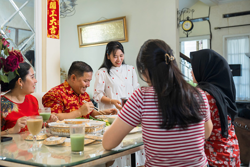 An extended family sitting at a dining table and eating a meal during Chinese New Year at home