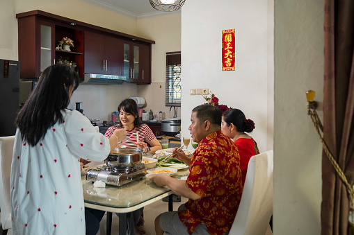 An extended family sitting at a dining table and eating a meal during Chinese New Year at home