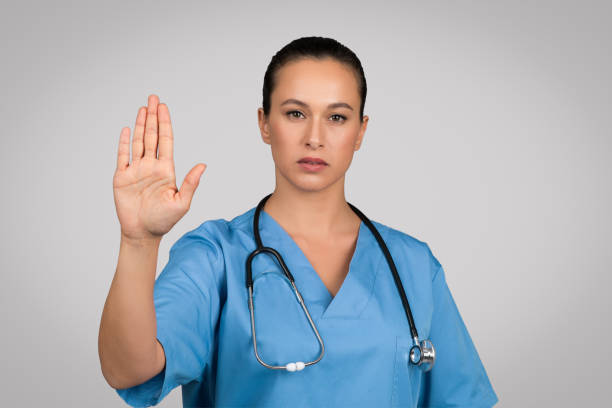 istock Serious european female doctor in blue uniform showing stop gesture, refusing something, saying no to viruses 1995278643