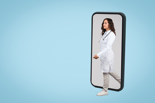 Confident female doctor stepping forward from a smartphone frame, depicting innovation in telehealth and digital healthcare services, blue background