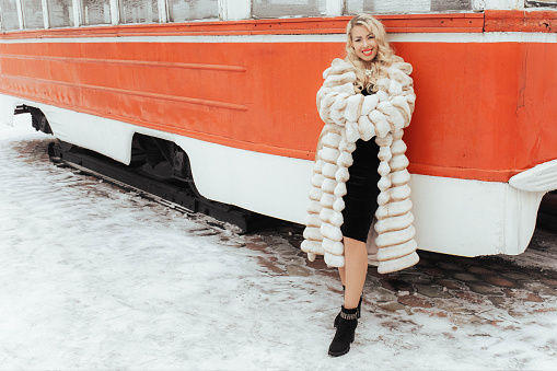 A beautiful girl in a fur coat in a red tram