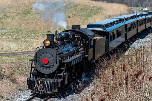 A Front and Slightly Above View of an Approaching Restored Narrow Gauge Passenger Steam Train Blowing Smoke and Steam on a Sunny Winter Day