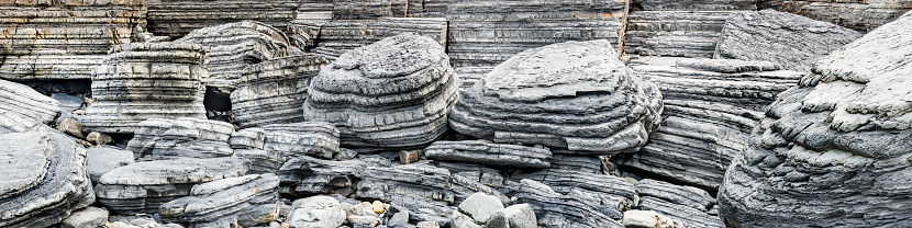 A breathtaking wide panoramic photograph showcasing the natural strata in large coastal boulders near Aberystwyth. This image is the perfect banner for nature enthusiasts and coastal lovers.