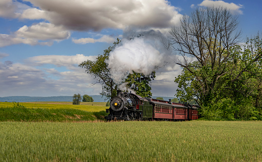 A View of an Antique Steam Passenger Train Approaching, Traveling Thru Rural Countryside, Blowing Smoke, on a Sunny Spring Day