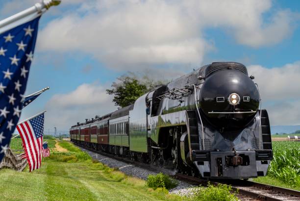 istock Streamlined Steam Passenger Train Passing a Fence, in the Countryside With American Flags Blowing 1995298071