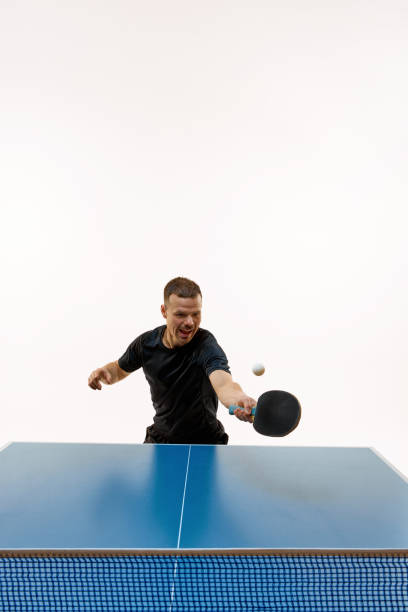 istock Table tennis player in black sport uniform striking ball with intensity against white studio background. Copy space. 1995308044