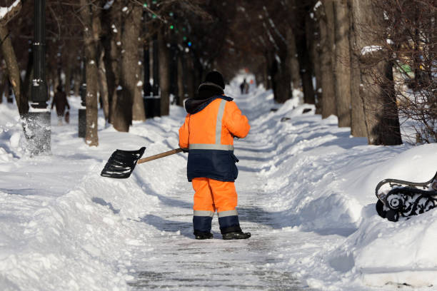 Communal services worker in uniform with a shovel clears snow on sidewalk