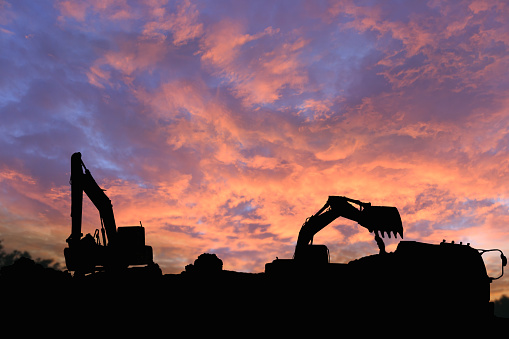 Crawler excavators silhouette are digging the soil in the construction site. on  sky cloud background