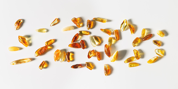 Natural Amber texture background, yellow orange colored stones with shadows on white. Natural gemstone mineral material for jewelry. Transparent pieces gem Amber scattered on white, top view banner