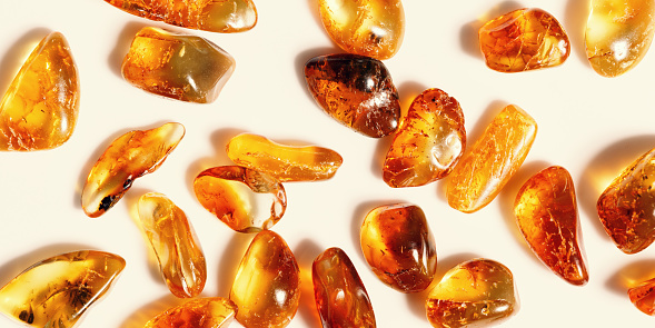 Natural gemstones of amber as background, transparent stones yellow orange colors. Natural rocks beige monochrome. Top view Amber textured gems. Aesthetic wallpaper, banner with uncut and raw stones.