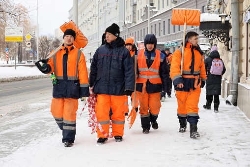 Moscow, Russia - February 8, 2024: Workers with shovels walking on a street, snow removal in winter city