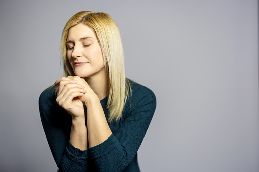 Portrait of beautiful woman with her eyes closed against grey background, Thoughtful young blonde in studio.