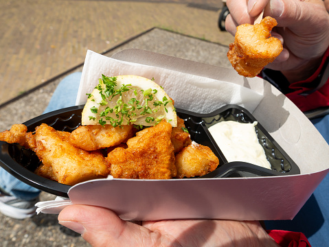 Eating fried codfish nuggets with a slice of lemon and mayonnaise from a cardboard tray, Netherlands