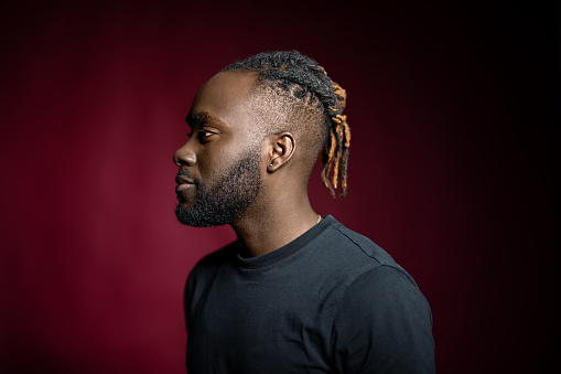 Profile portrait of African American man with beard and braided hair in studio. Side view of a young man against red background.