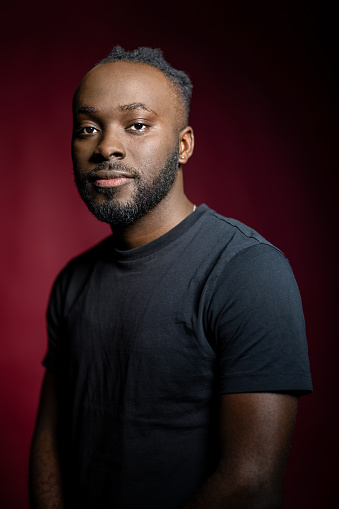 Portrait of handsome young african man staring at camera. African male in black t-shirt with blank expression on red background.