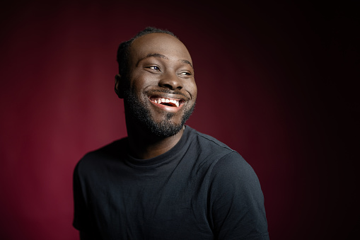 Cheerful young man against red background. African man in casuals standing in studio and laughing.