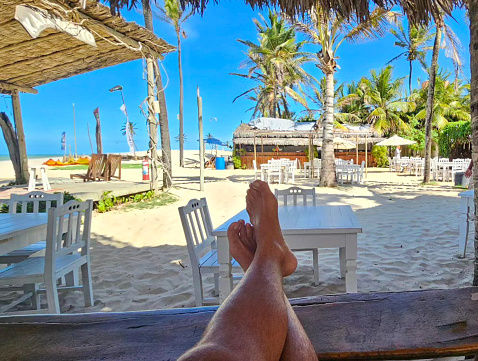 Sandy toes and feet of a couple on lounge chairs enjoying a beach vacation while watching their kids play in the sand. Tropical resort setting