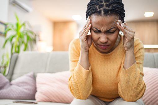 Black woman massaging her head while experiencing painful migraine at home