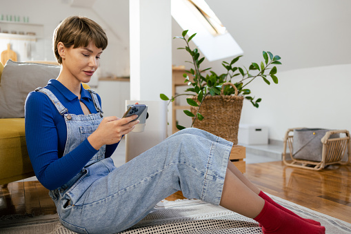 Portrait of a young woman relaxing at home and using smartphone.