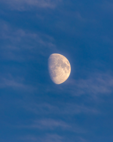 Hazy Waxing Gibbous moon surrounded by wispy clouds just after sunset in a deep blue sky