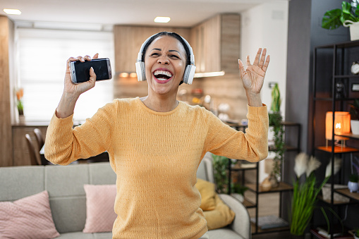 Smiling black woman with wireless headphones having fun listening to music at home