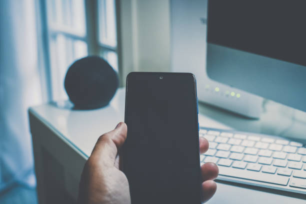Smartphone in hand. Speaker, router, computer on desk. Technology, domotics, home automation concept