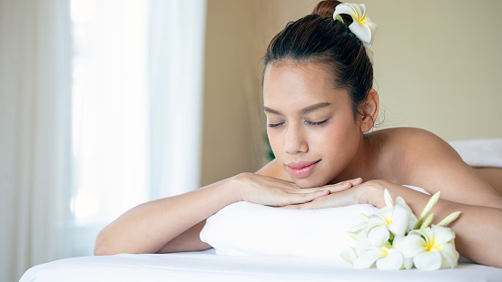 A tranquil spa experience is beautifully portrayed as an attractive Asian woman enjoys a salt spa treatment, embodying wellness and beauty with a serene smile on a white bed with copy space