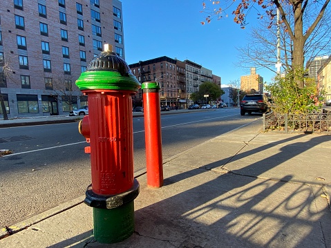 New York, NY USA - November 28, 2023 : Fire hydrant painted in the pan-African flag colors of red, green and black creating a long shadow on the sidewalk on Malcolm X Boulevard aka Lenox Avenue in Harlem, New York City
