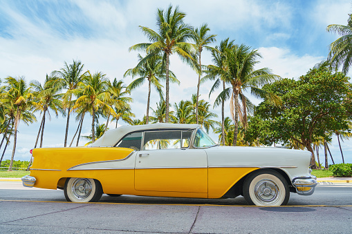 Yellow classic car on a tropical beach with palm tree, vintage process