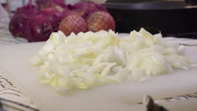 White onion sliced, diced with knife on cutting board by gloved hands