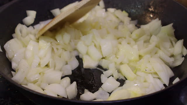 Close up: Wooden spoon stirs diced onions frying in hot cast iron pan