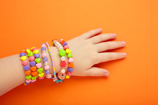 Child wears bracelets on his hands. Kids handmade beaded jewelry on orange background. Top view