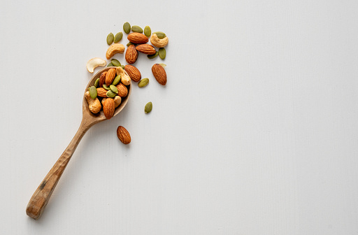 Mix of nuts. Almonds, cashews and pumpkin seeds in a wooden spoon are scattered on a white wooden background. Healthy energy snack concept. Top view and copy space.